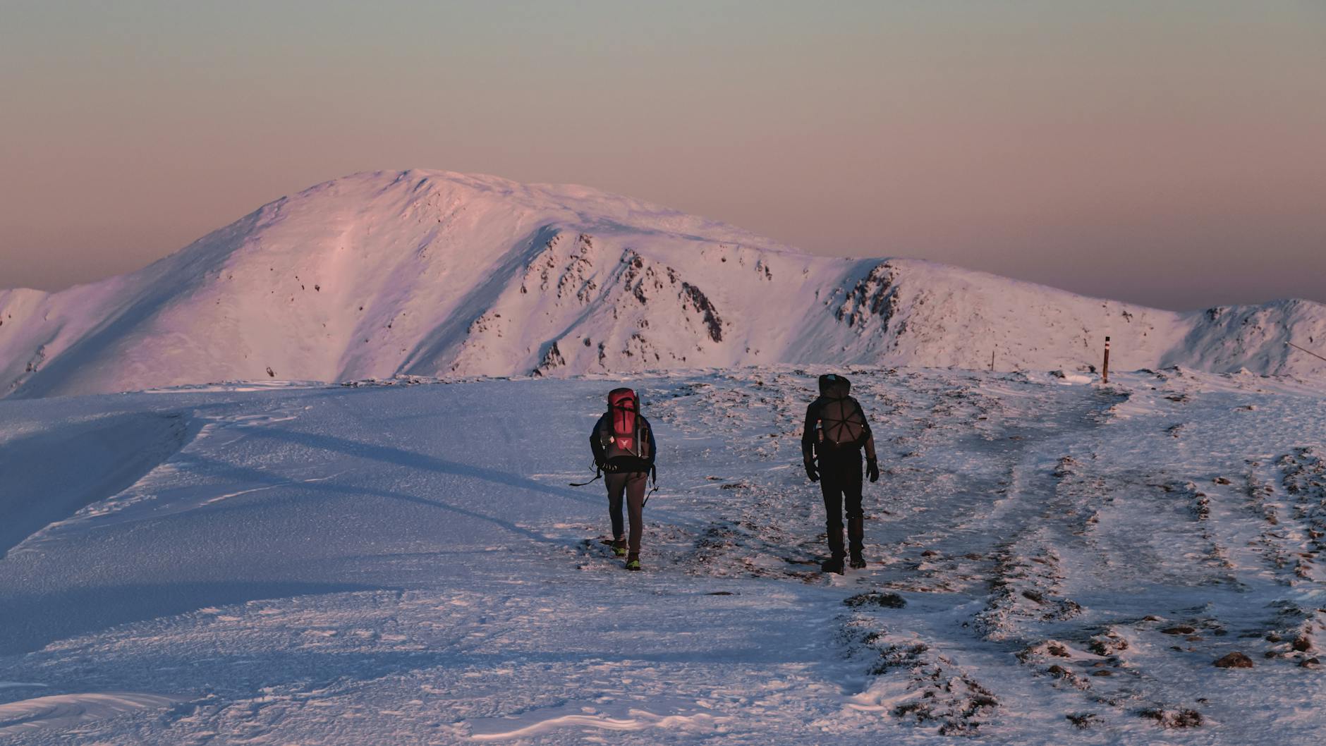 Dwóch turystów idzie o zachodzie słońca po ośnieżonych czeskich górach