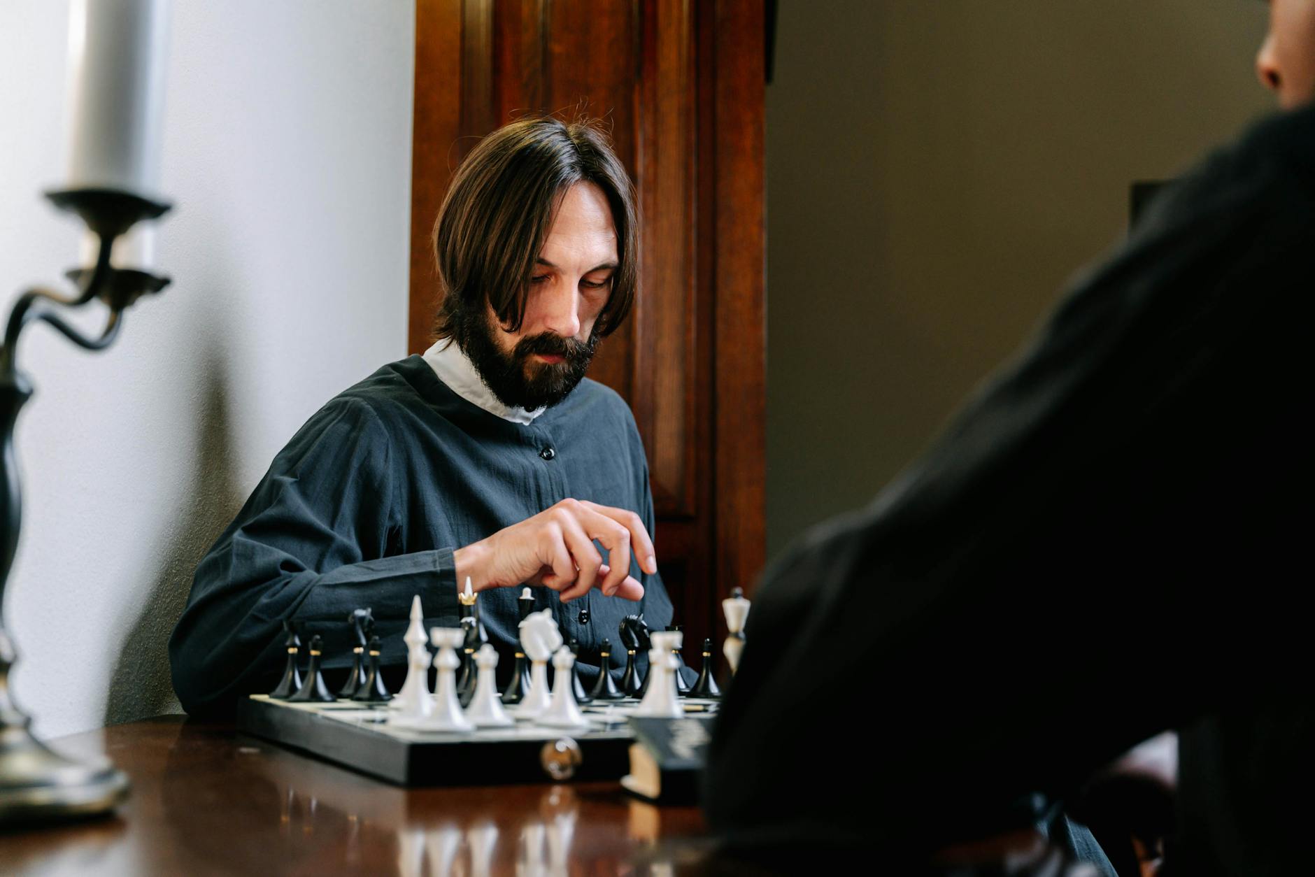 Brodaty mężczyzna zamyślony nad partią szachów przy drewnianym stole