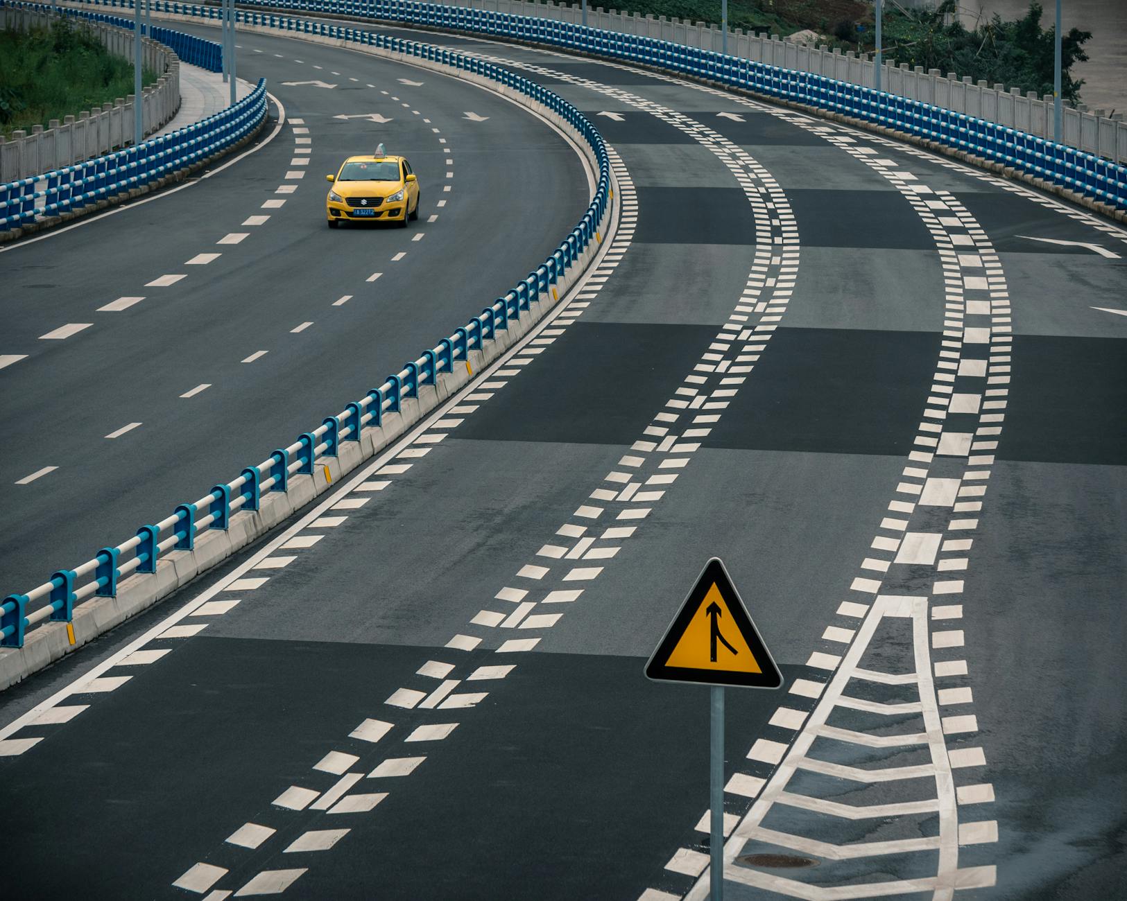 Żółta taksówka jedzie po pustej, zakrzywionej autostradzie z pasem włączania