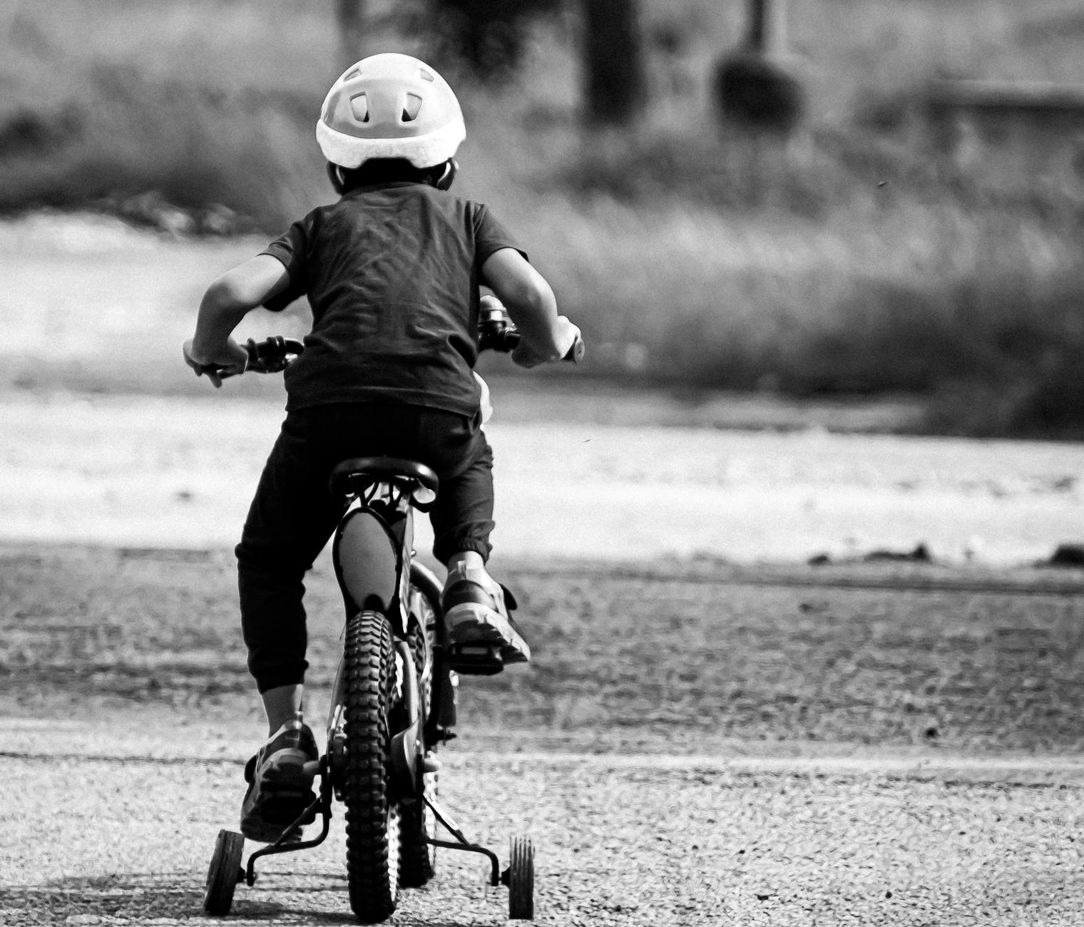 Dziecko w kasku jedzie na rowerze z bocznymi kółkami po pustej drodze
