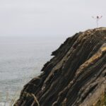 Kobieta w bieli stoi na skraju klifu nad wzburzonym oceanem