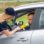 Policjant bada alkomatem kierowcę stojącego przy samochodzie